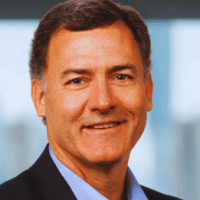 Head-and-shoulders portrait of a smiling middle-aged man in a dark blazer and light blue shirt, office setting.